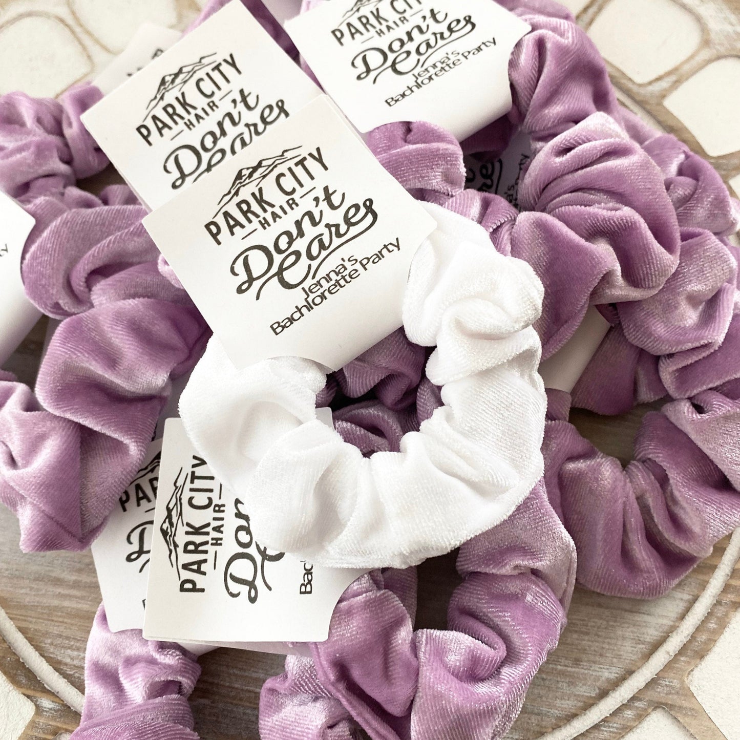 Purple scrunchies with 'Park City Hair Don't Care' labels on a textured surface
