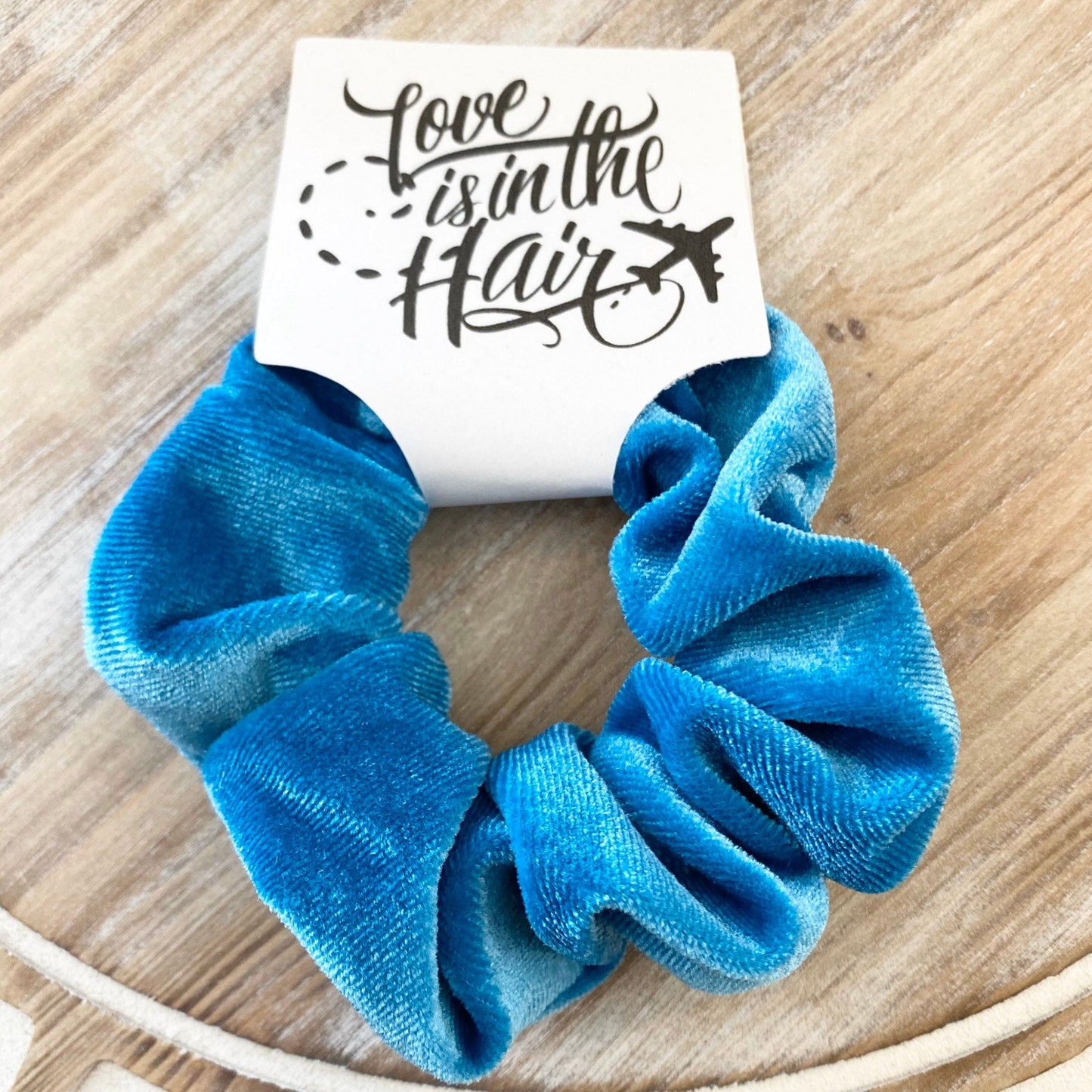 Blue scrunchie on a wooden surface with a card that says 'Love is in the Hair'.