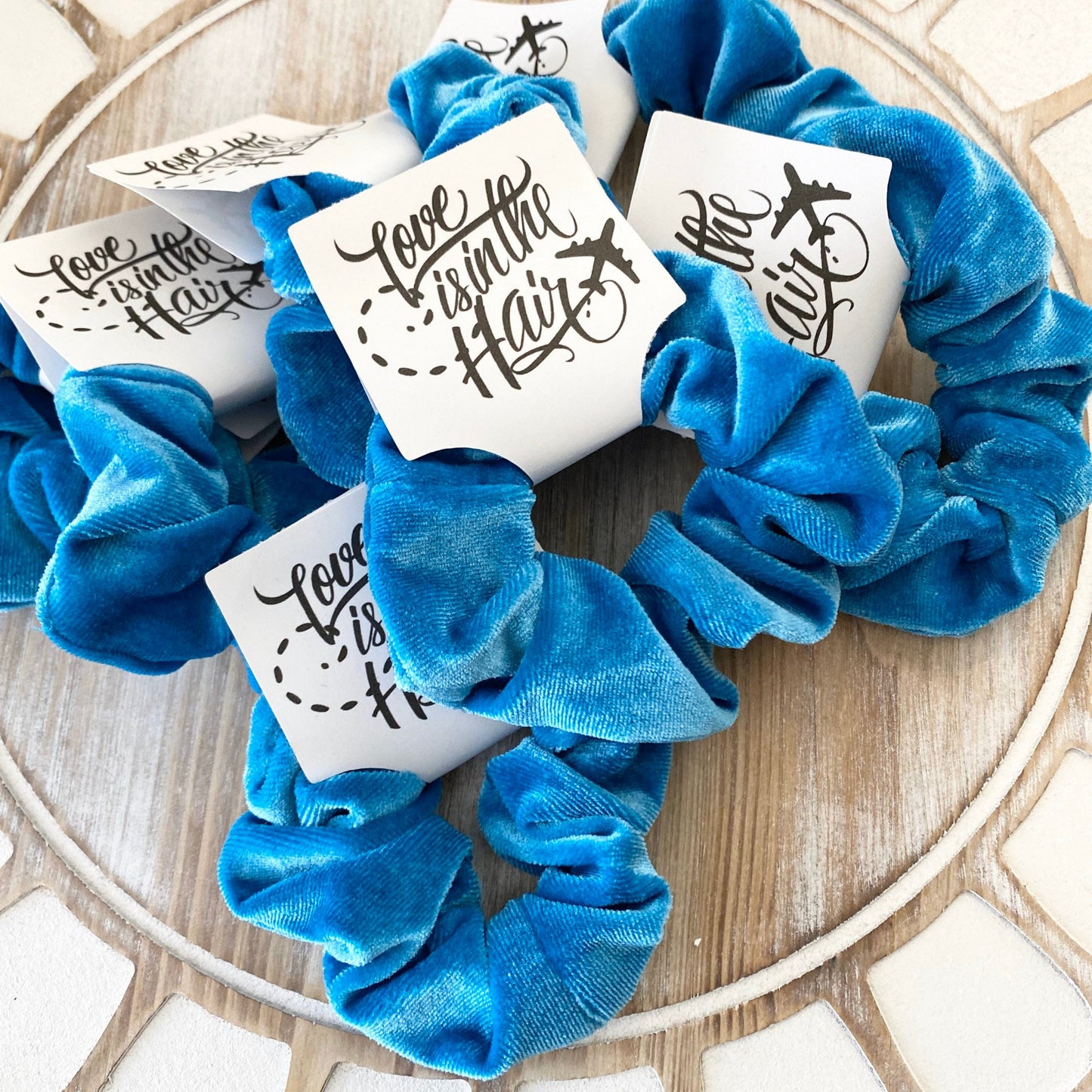 Blue scrunchies with 'Love is in the Hair' cards on a wooden surface