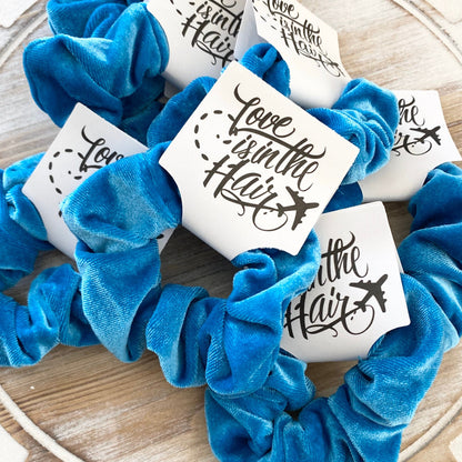 Blue scrunchies with 'Love is in the Hair' stickers on a wooden surface