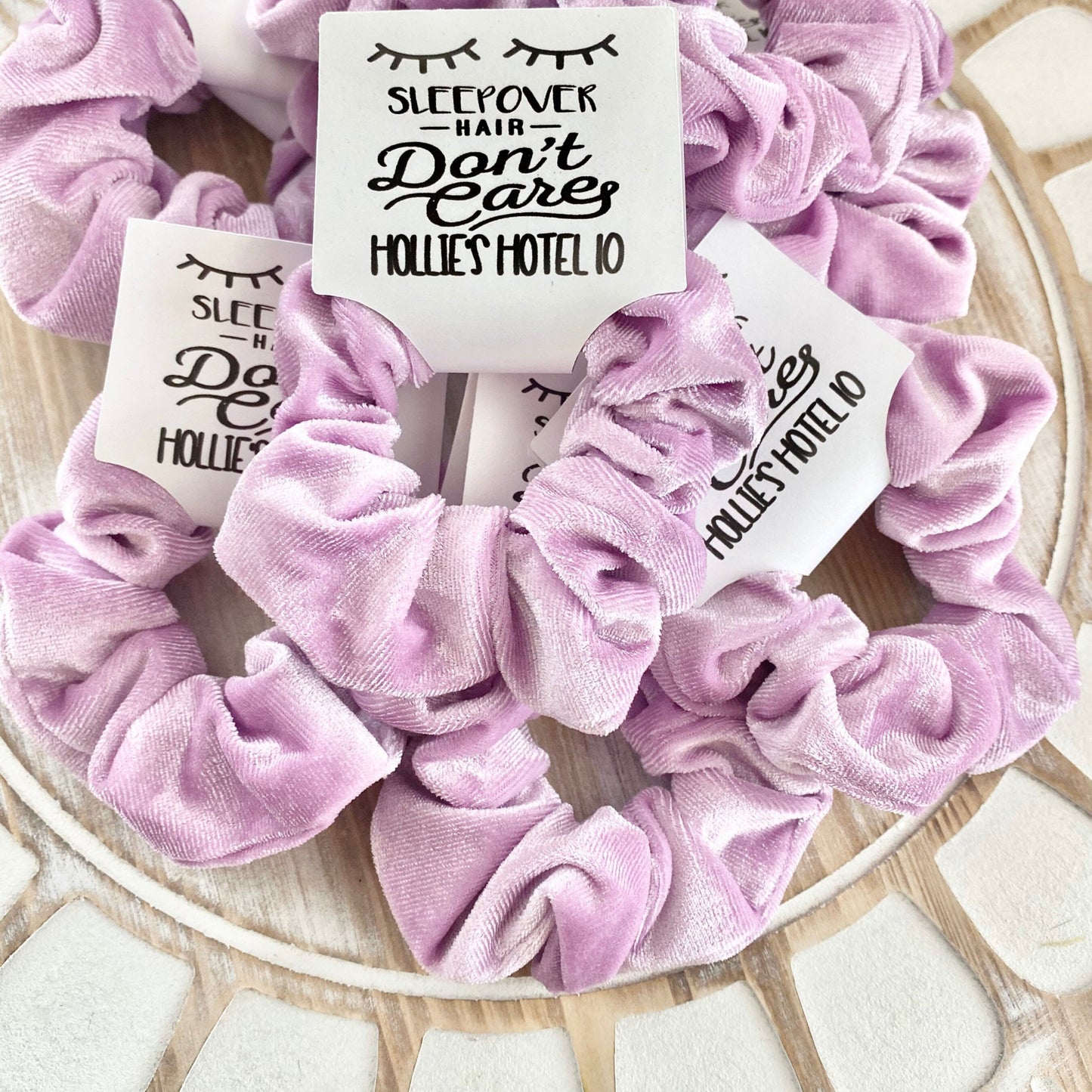 Lavendar scrunchies with 'Sleepover Hair Don't Care Hollie's Hotel 10' labels on a wooden surface.