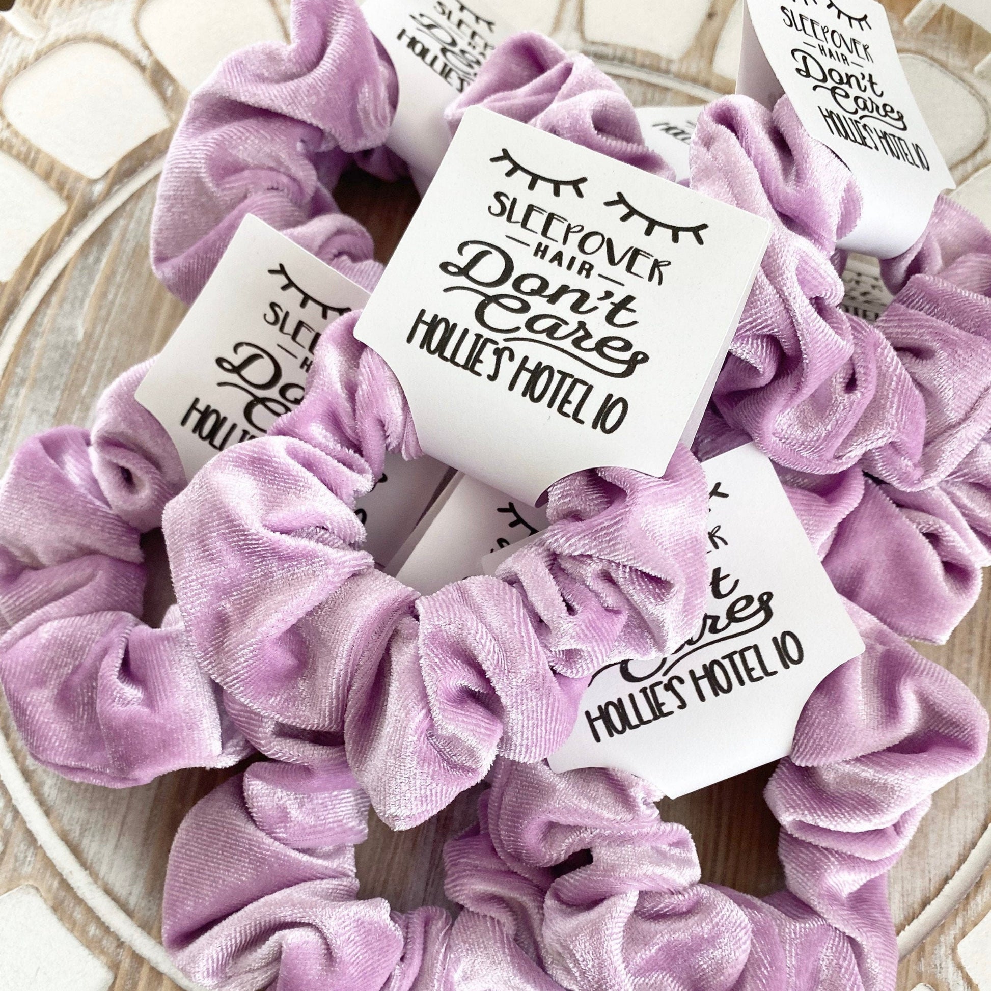 Set of purple scrunchies with personalized labels on a wooden surface