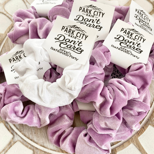 Purple scrunchies with white labels on a decorative surface