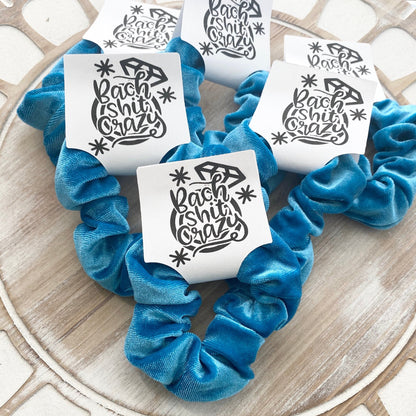 Blue scrunchies with 'Bach Shit Crazy' text on a wooden surface