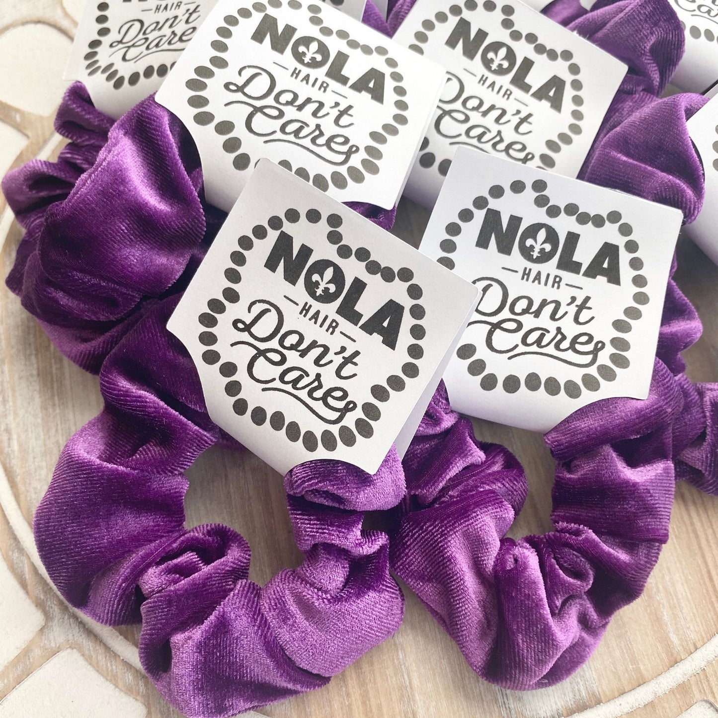 Purple scrunchies with 'NOLA Hair Don't Care' labels on a wooden surface