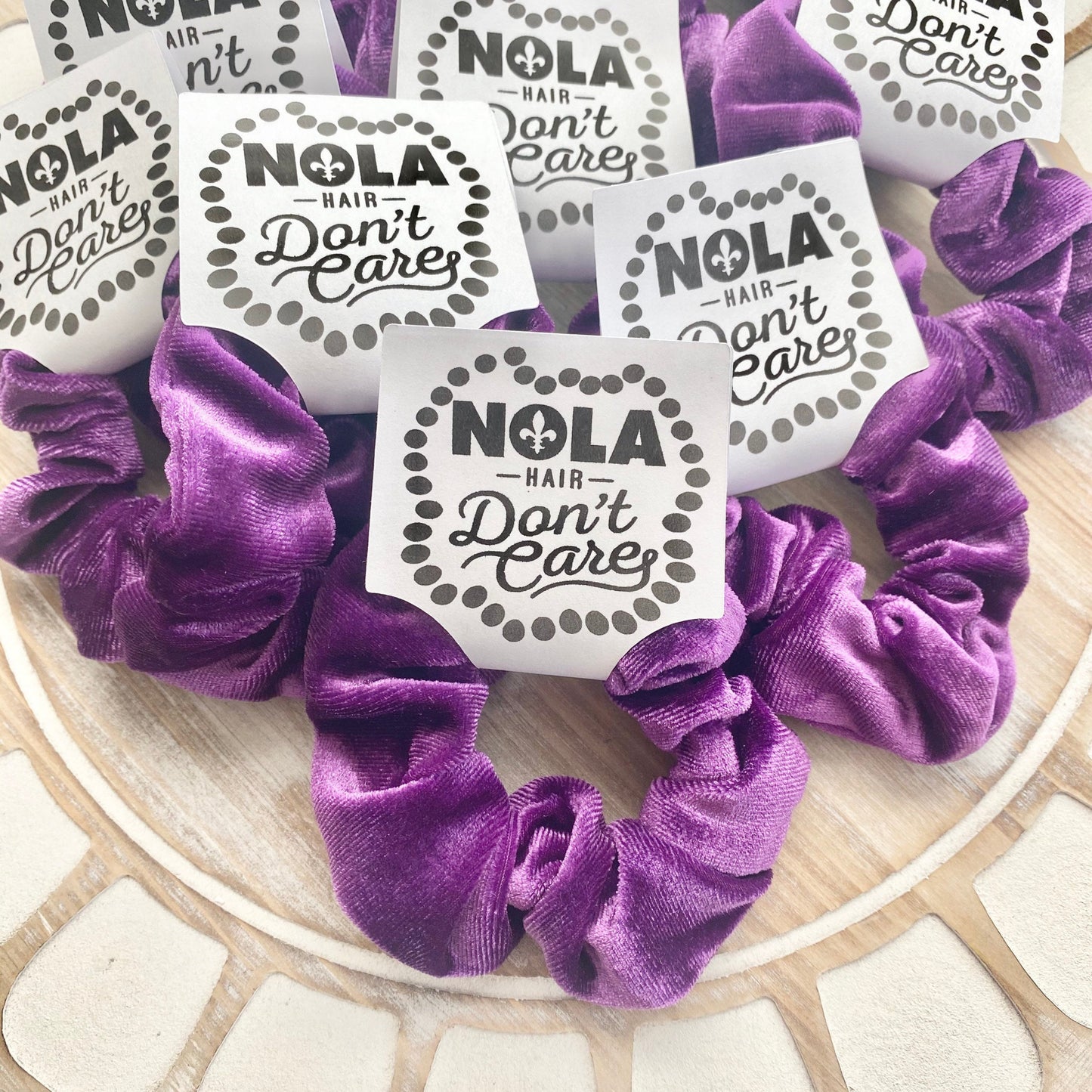 Purple scrunchies with 'NOLA Hair Don't Care' labels on a decorative plate.