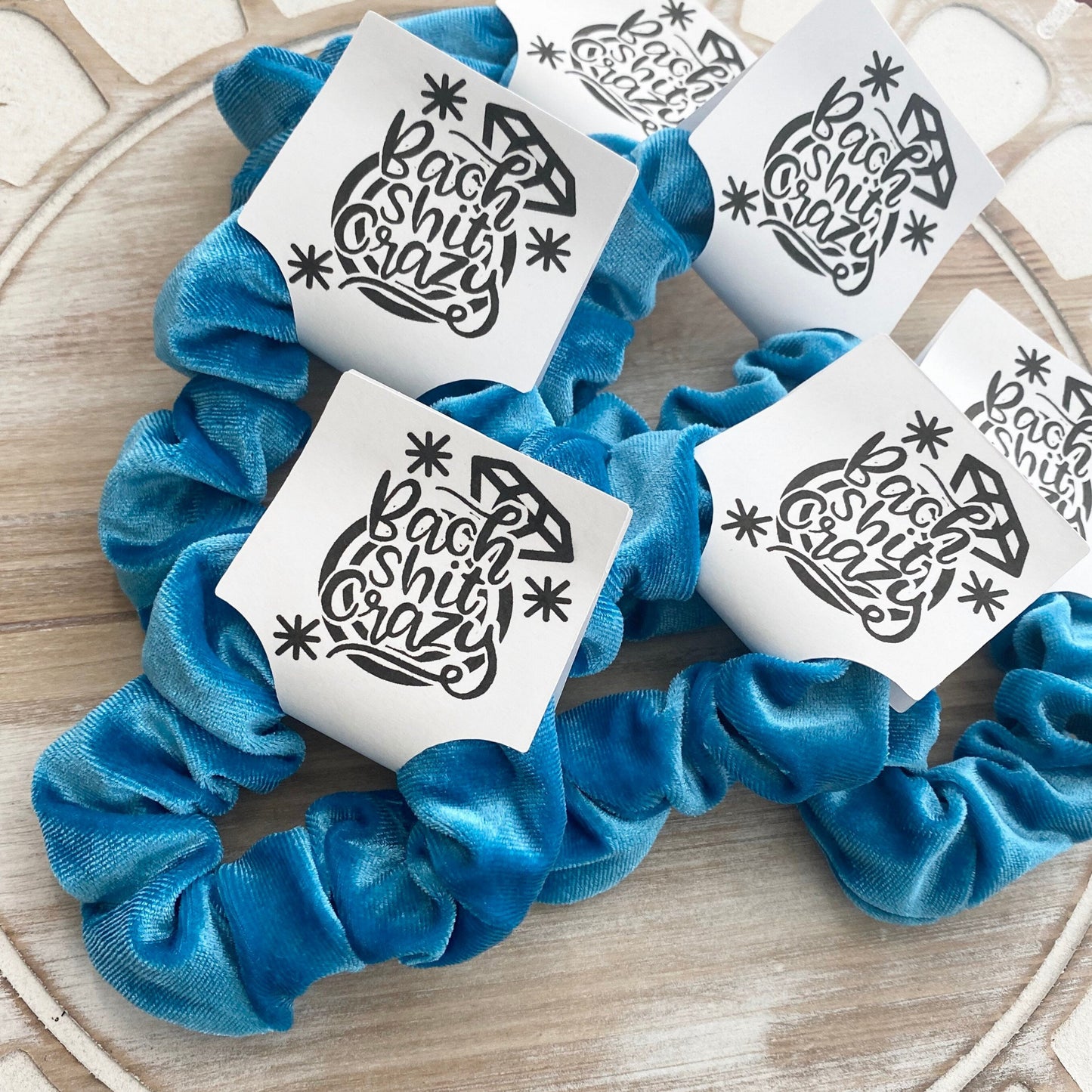 Blue scrunchies with white cards featuring black text on a wooden surface
