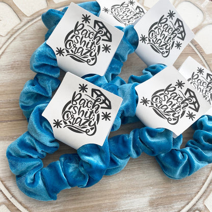 Blue scrunchies with white cards featuring black text on a wooden surface