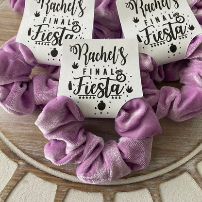 Purple scrunchies with 'Rachel's Final Fiesta' labels on a wooden surface