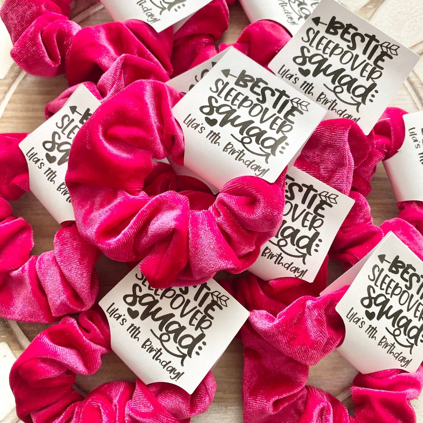 Pink scrunchies with personalized labels on a wooden surface