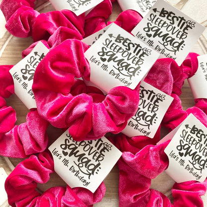 Pink scrunchies with personalized labels on a wooden surface