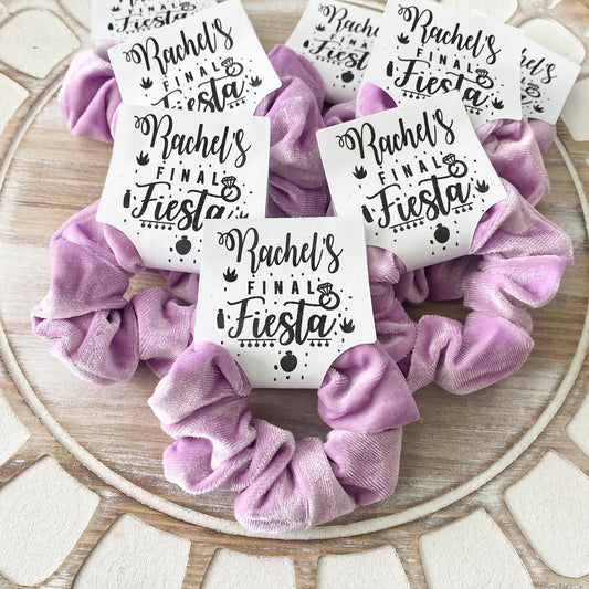 Purple scrunchies with 'Rachel's Final Fiesta' labels on a wooden surface