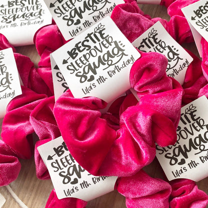 Pink scrunchies with personalized labels on a wooden surface