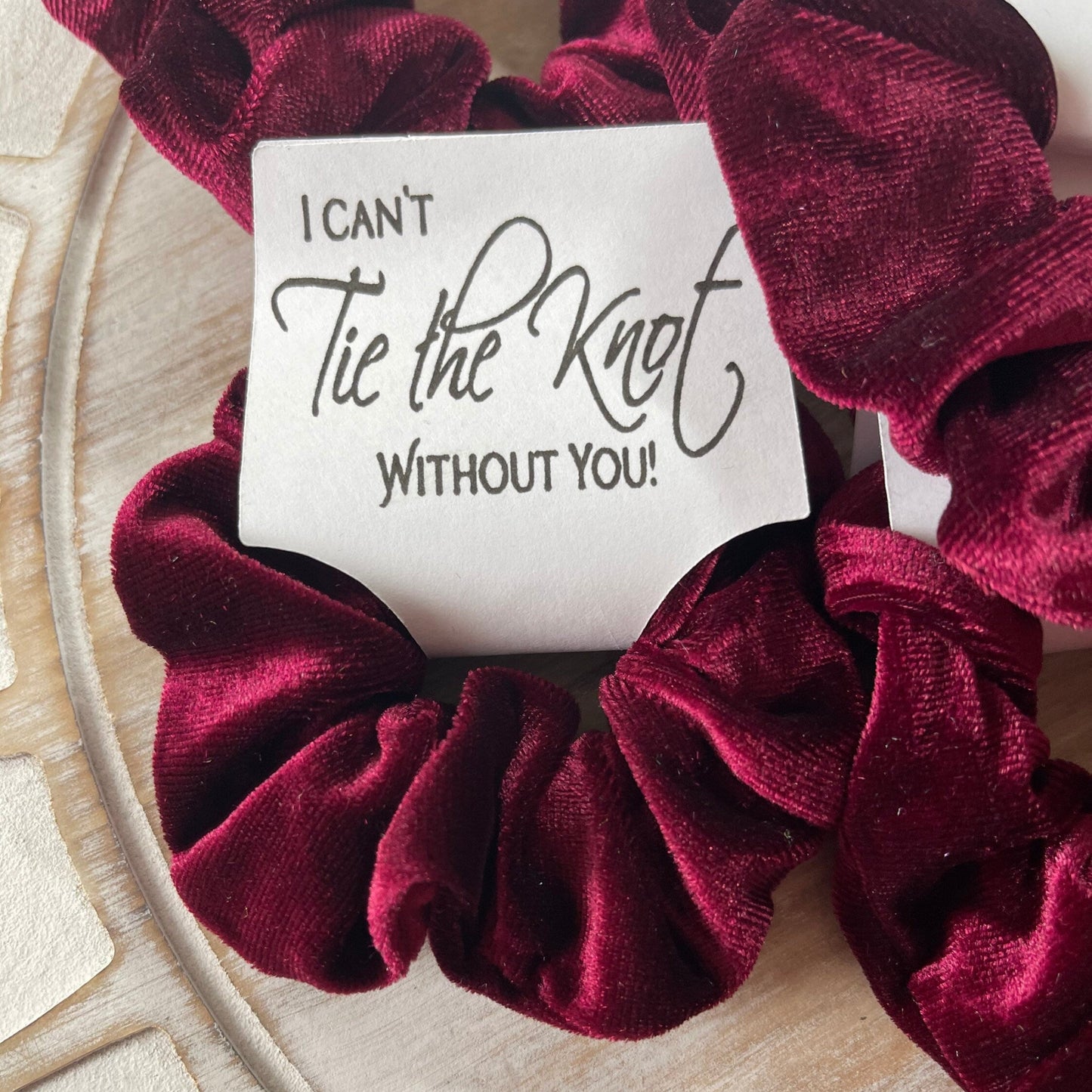 Maroon scrunchie with a card inside on a wooden surface