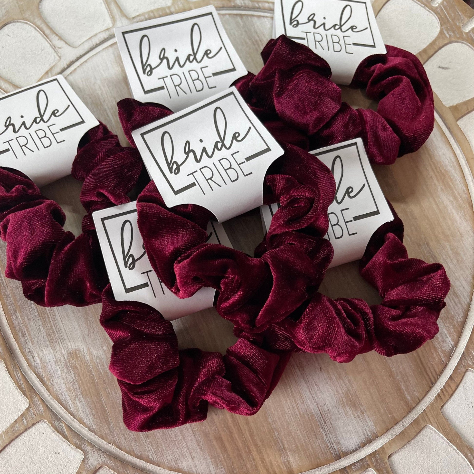 Burgundy scrunchies with 'Bride Tribe' labels on a wooden surface