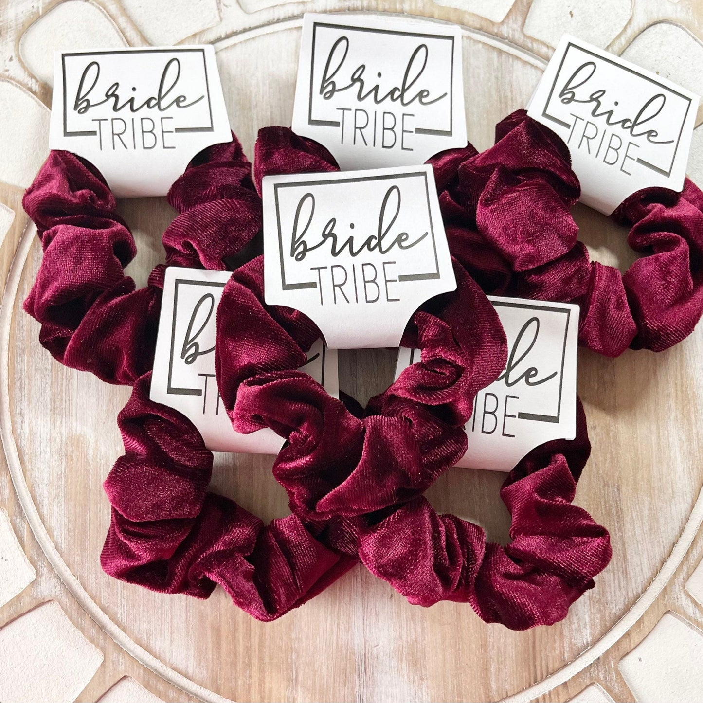 Burgundy scrunchies with 'bride tribe' labels on a decorative surface