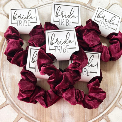 Burgundy scrunchies with 'bride tribe' labels on a decorative surface