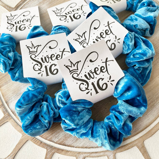 Blue scrunchies with 'sweet 16' labels on a decorative surface