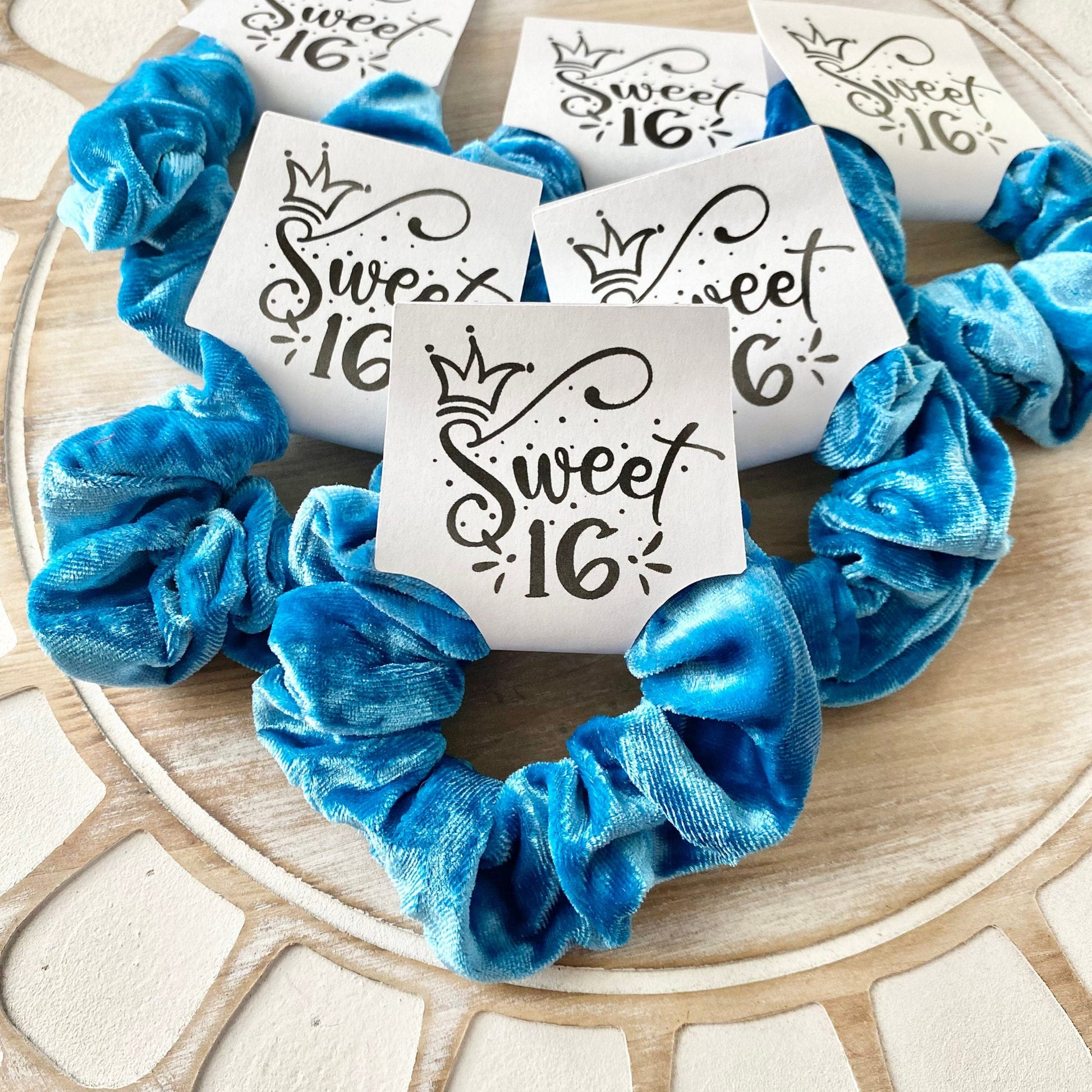 Blue scrunchies with 'Sweet 16' labels on a wooden surface