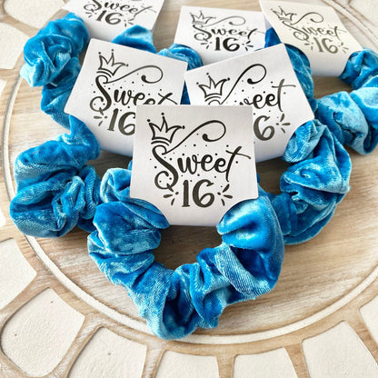 Blue scrunchies with 'Sweet 16' labels on a wooden surface