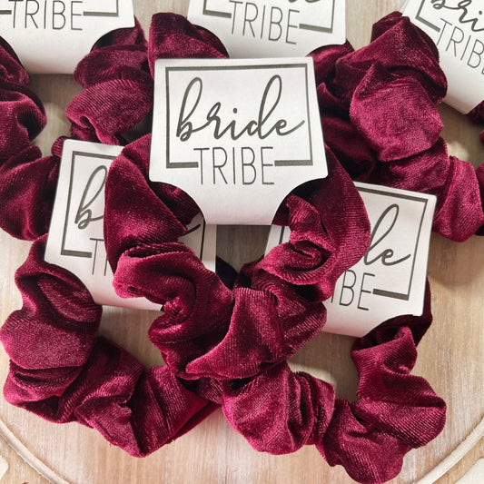 Burgundy scrunchies with 'bride tribe' labels on a wooden surface