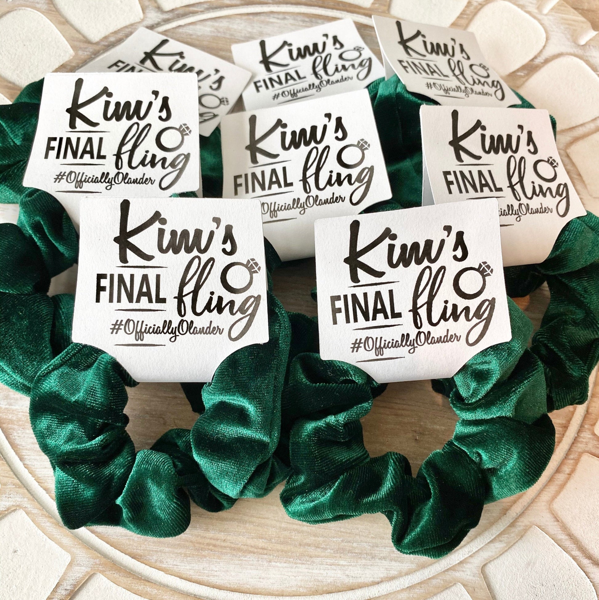 Green scrunchies with 'Kim's Final Fling' stickers on a wooden surface