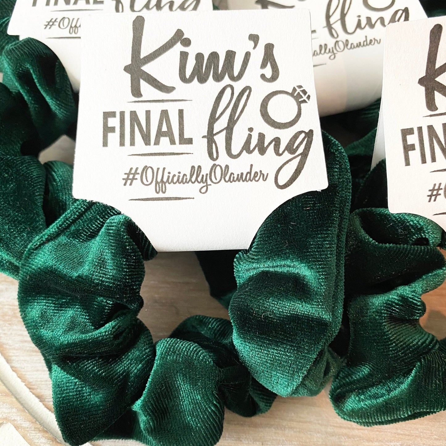 Green scrunchies with a 'Kim's Final Fling' label on a wooden surface