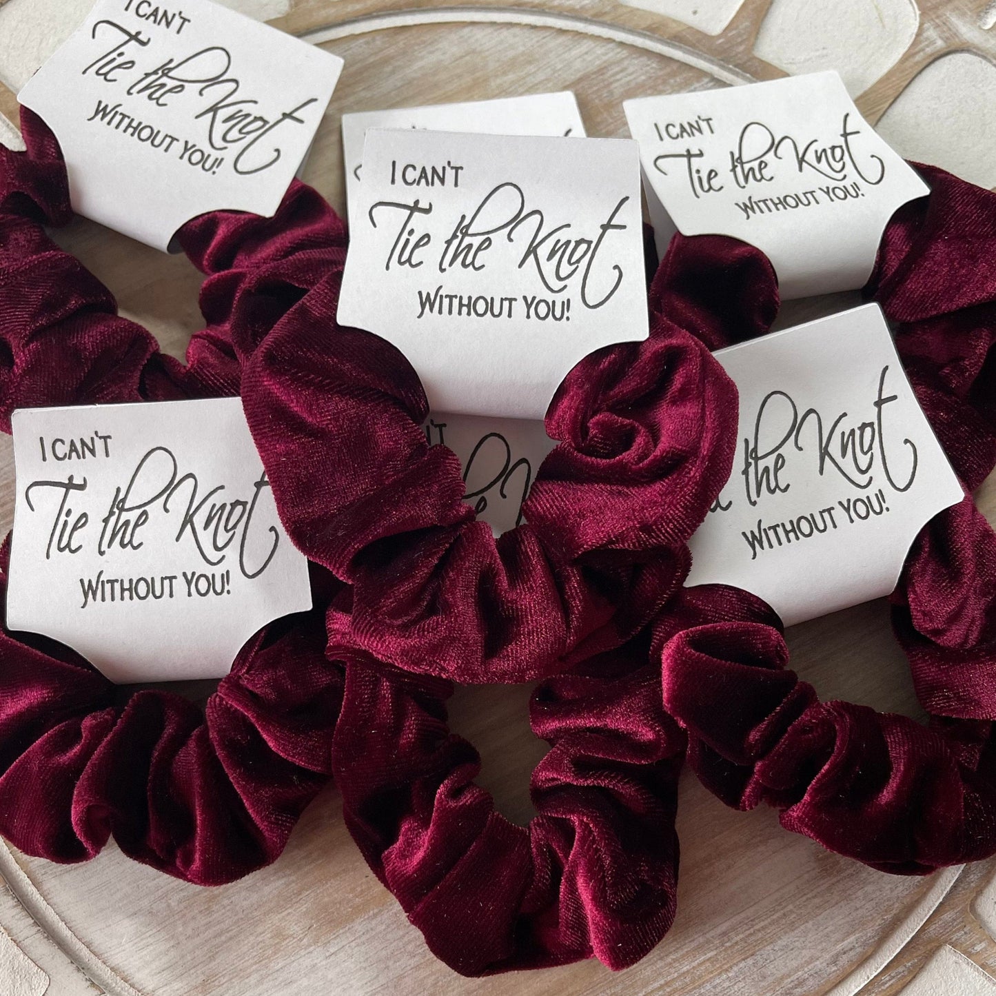 Maroon velvet scrunchies with 'I can't tie the knot without you' cards on a wooden surface.