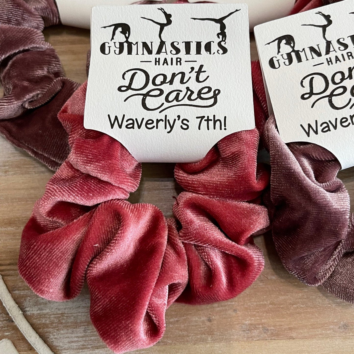 Velvet scrunchies with personalized 'Gymnastics Hair Don't Care' labels on a wooden surface