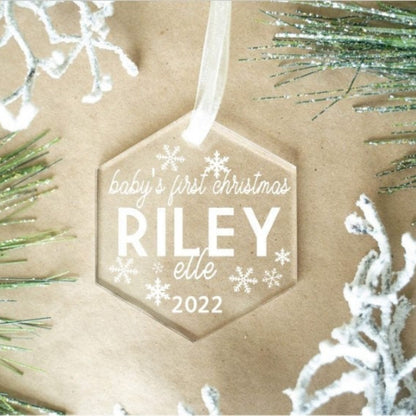 Hexagonal ornament with 'baby's first Christmas RILEY elle 2022' text on a brown paper background with decorative branches.