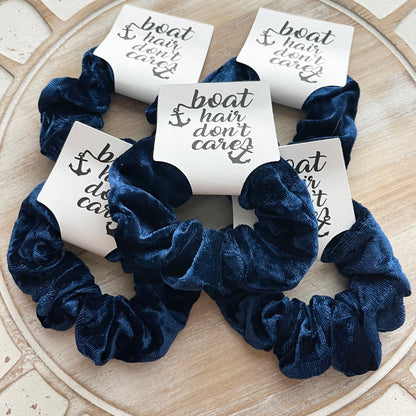 Navy blue scrunchies with 'boat hair don't care' cards on a stone surface