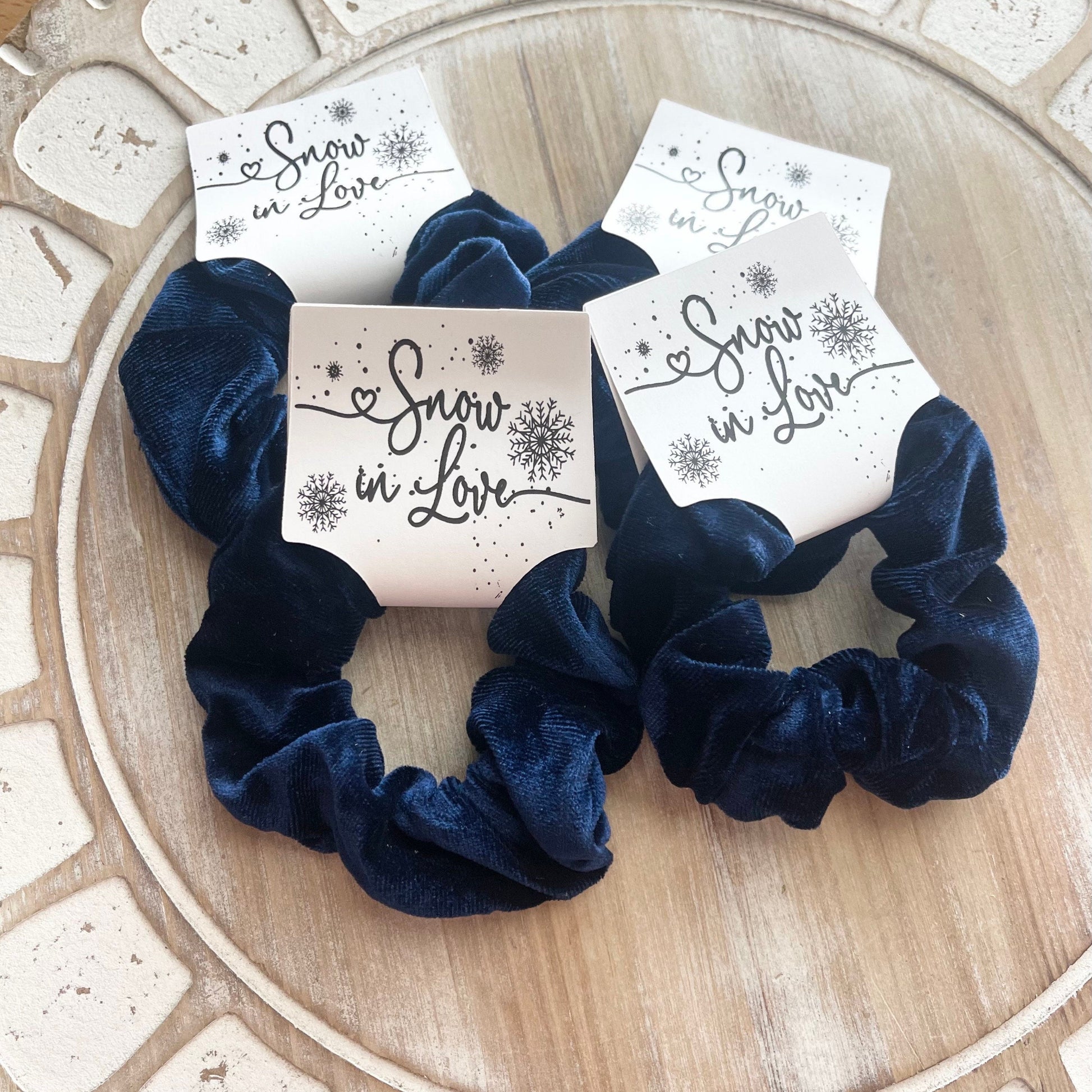 Navy blue scrunchies with 'Snow in Love' packaging on a wooden surface