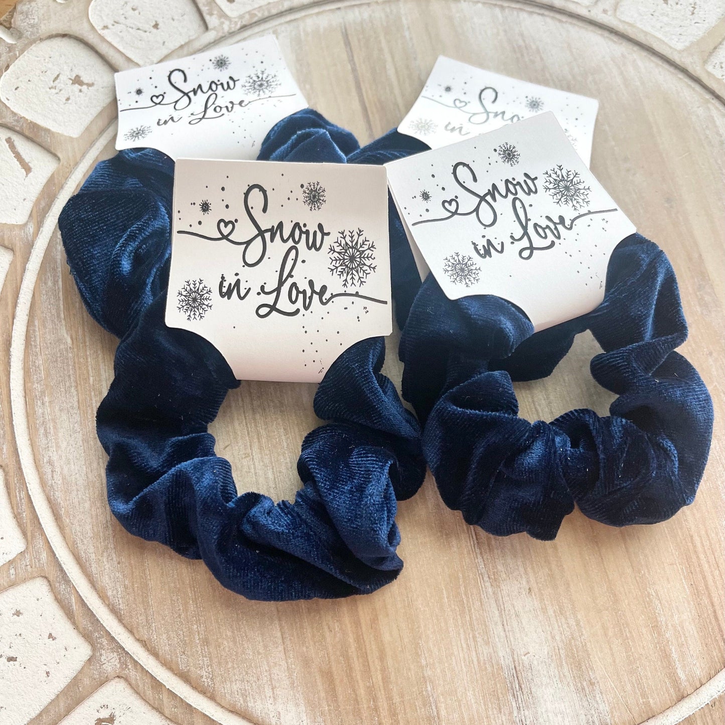 Navy blue scrunchies with 'Snow in Love' packaging on a wooden surface