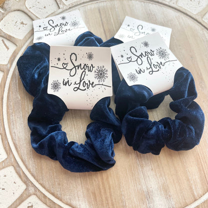 Navy blue scrunchies with 'Snow in Love' packaging on a wooden surface