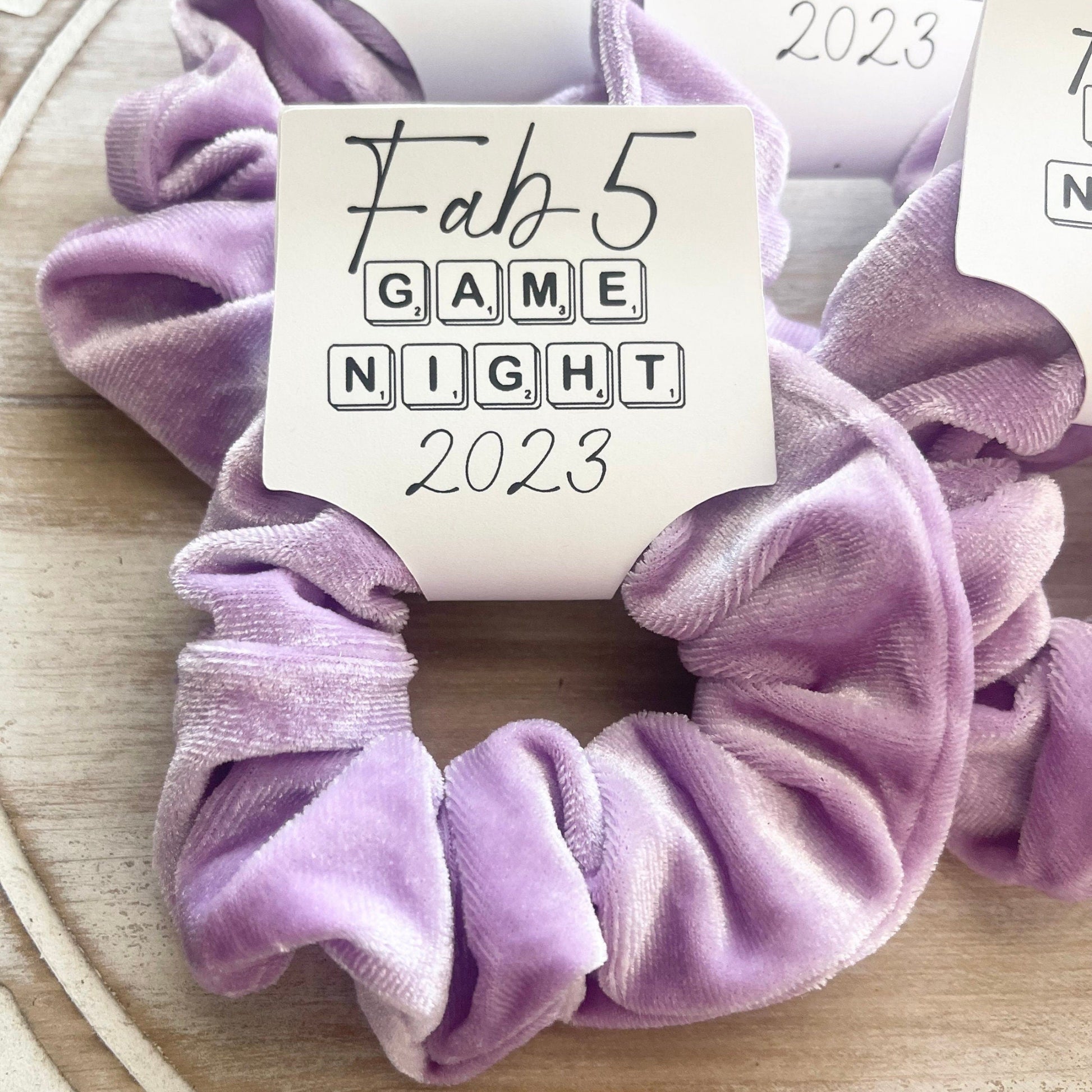 Purple scrunchie with 'Fab 5 Game Night 2023' label on a wooden surface