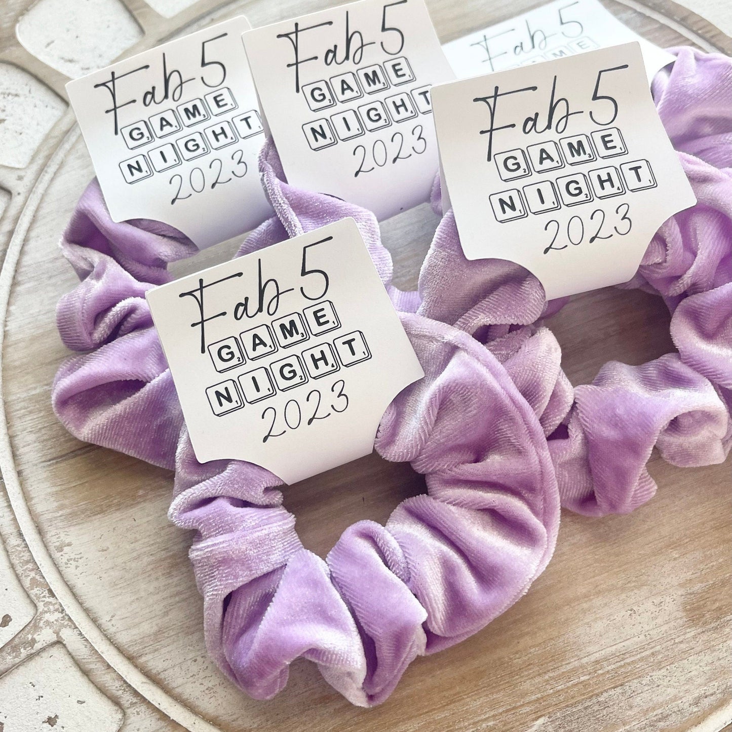 Purple scrunchies with 'Fab 5 Game Night 2023' labels on a decorative surface.