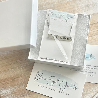 Silver necklace with engraved message in a Blue Eyed Jewels box on a wooden surface