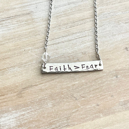 Silver necklace with 'Faith > Fear' pendant on a wooden surface