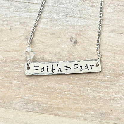 Silver necklace with 'Faith > Fear' pendant on a wooden surface