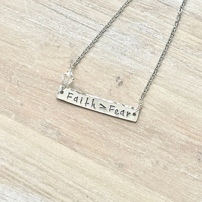 Silver necklace with 'Faith > Fear' pendant on a wooden surface