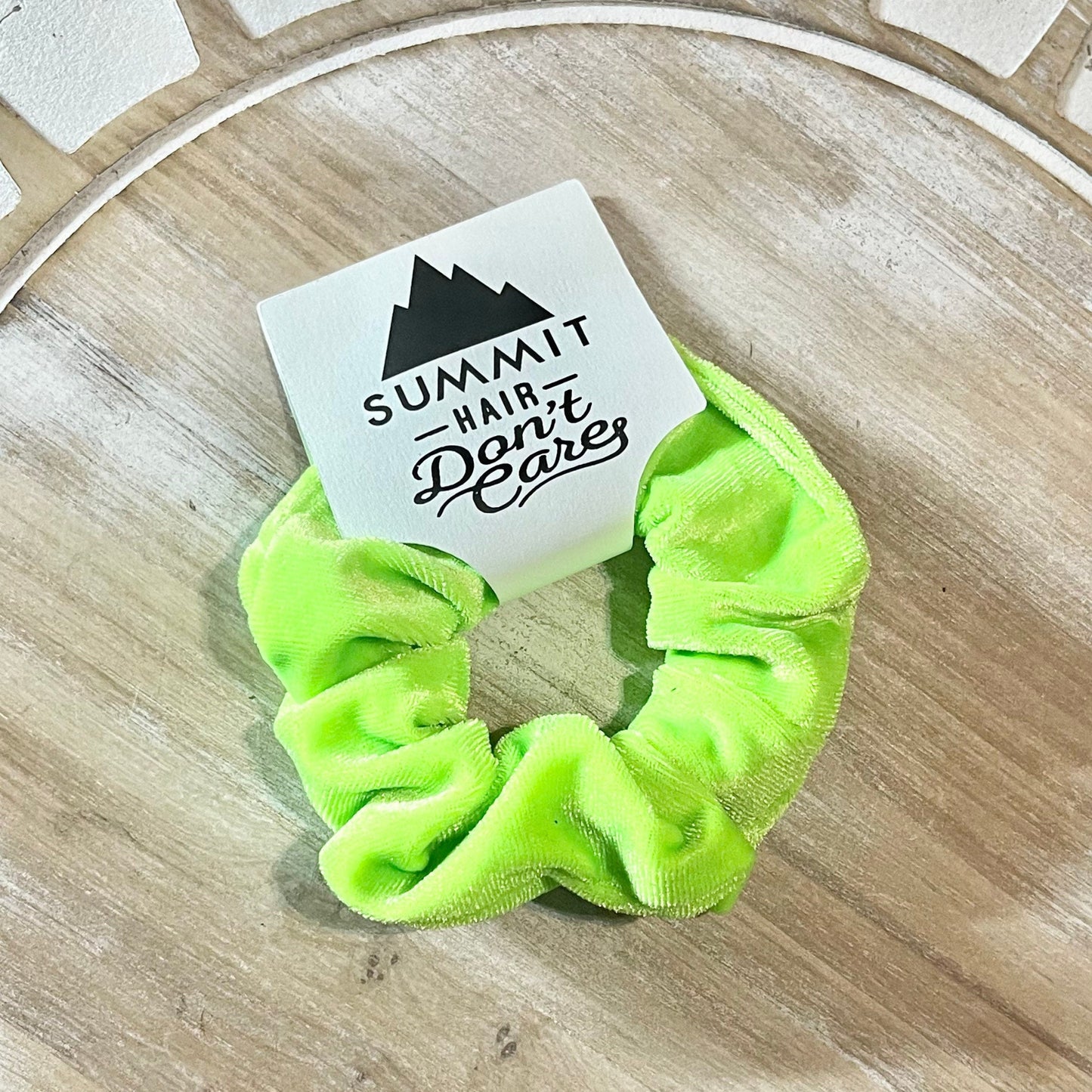Neon green scrunchie with a 'Summit Hair Don't Care' label on a wooden surface