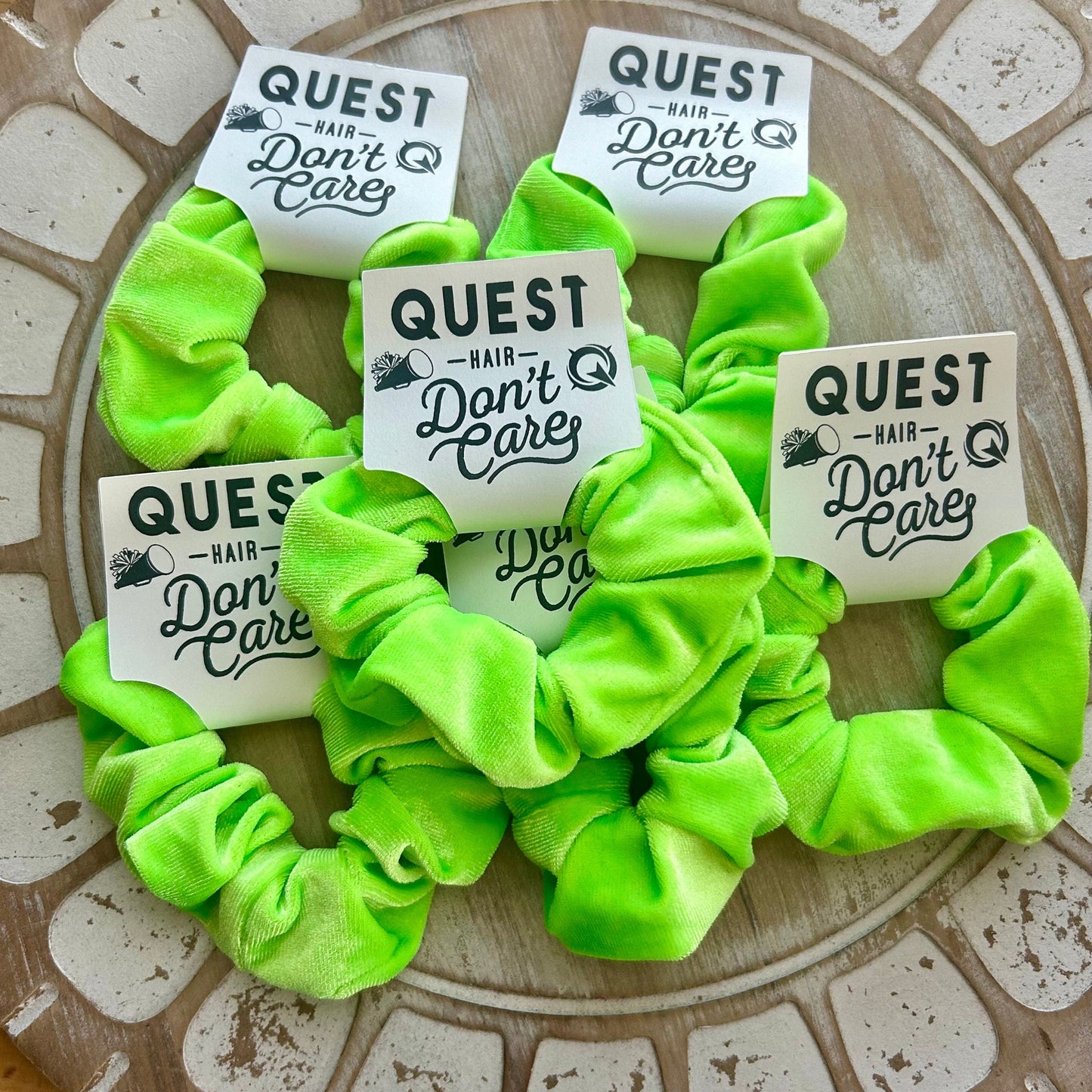 Neon green scrunchies with 'Quest Hair Don't Care' labels on a textured surface