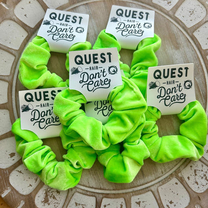 Neon green scrunchies with 'Quest Hair Don't Care' labels on a textured surface