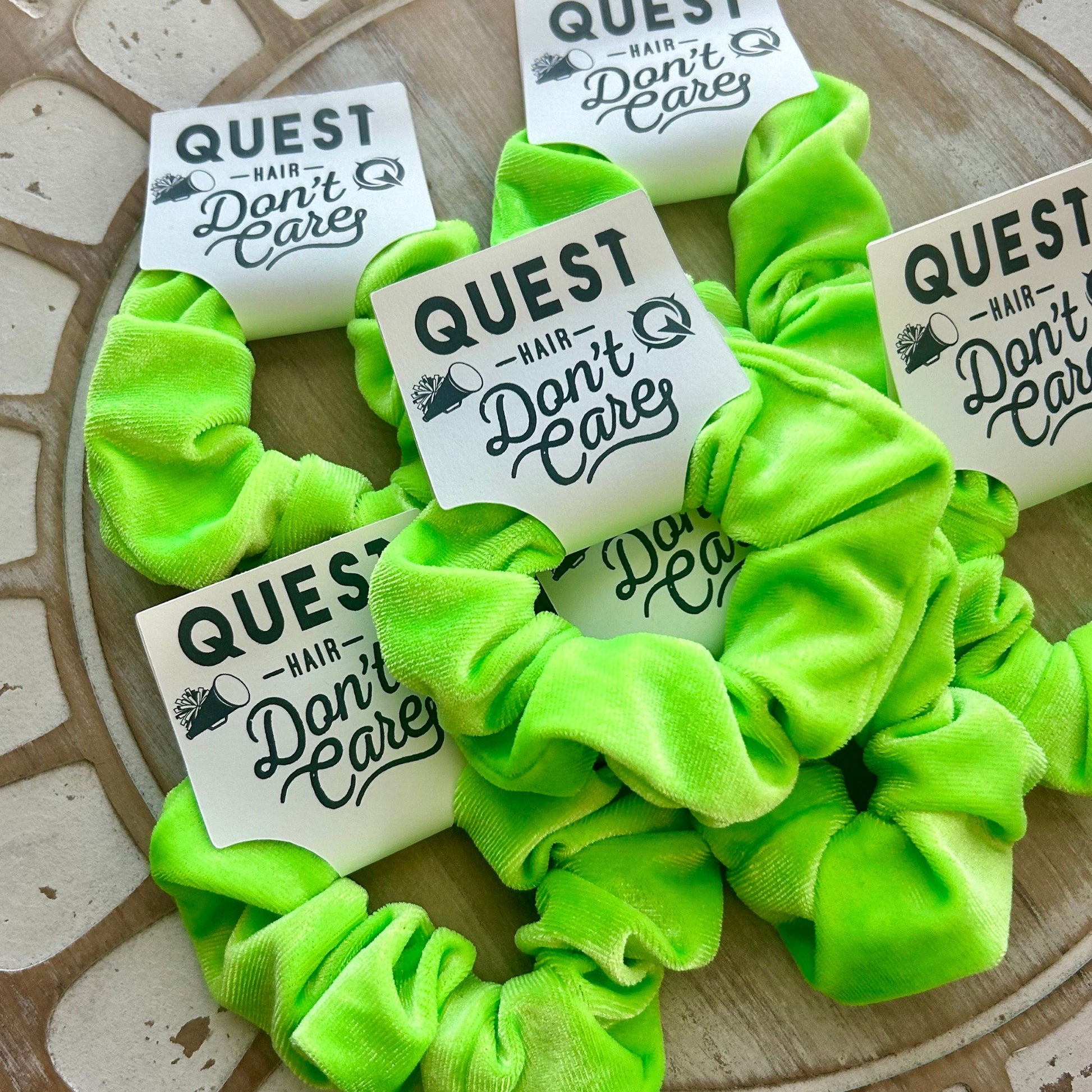 Green scrunchies with 'Quest Hair Don't Care' labels on a textured surface
