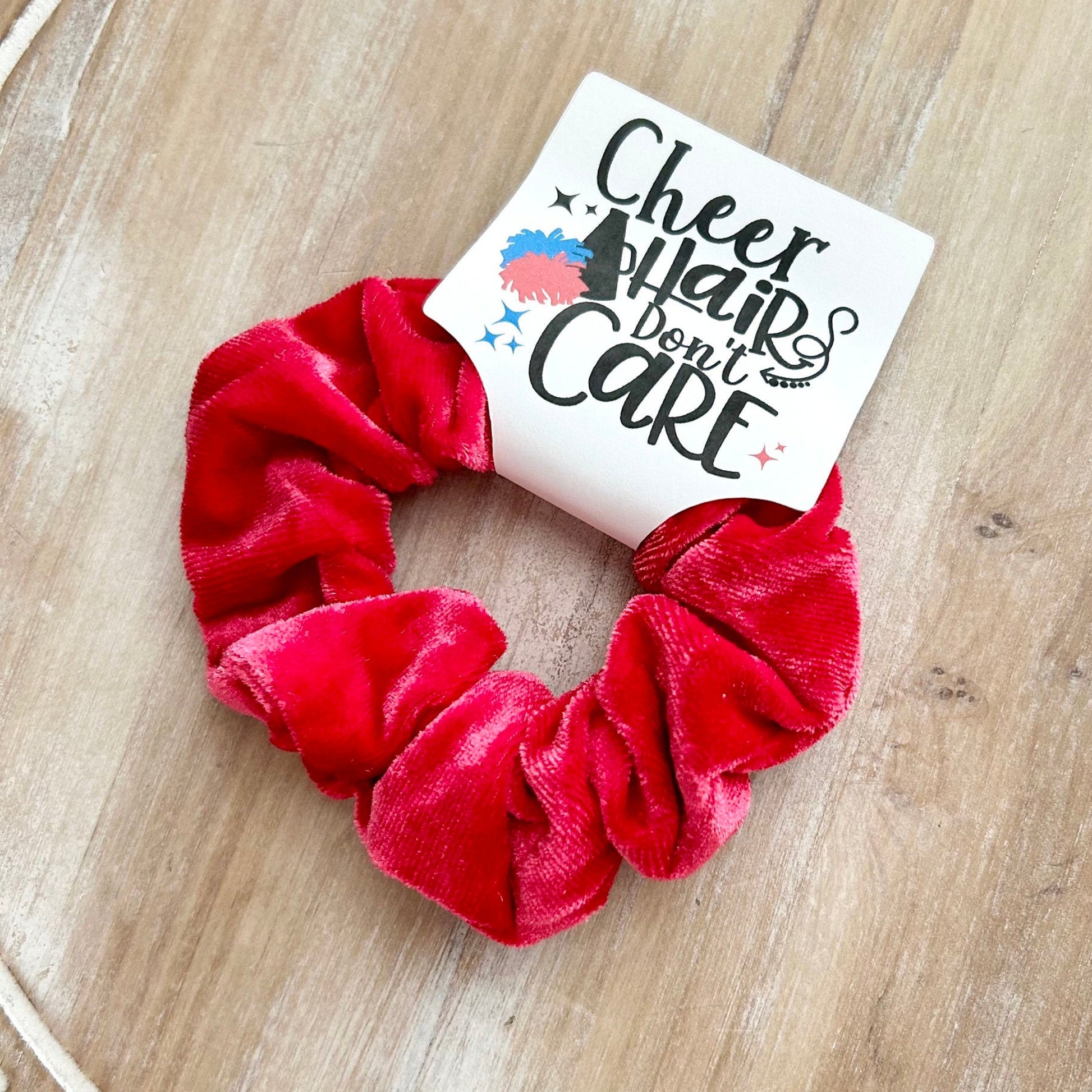 Red scrunchie with a card reading 'Cheer hair don't care' on a wooden surface