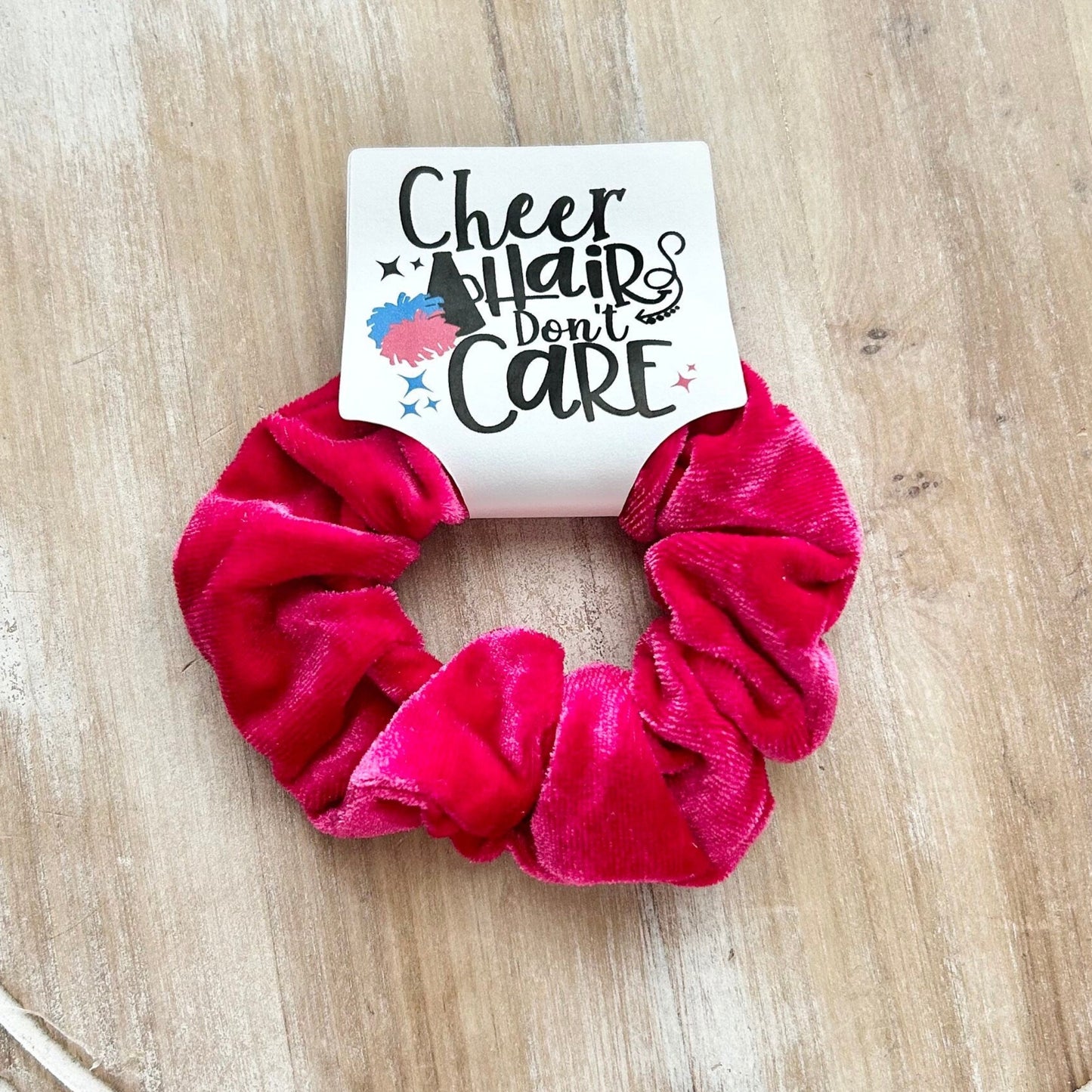 Pink scrunchie on a wooden surface with a card that says 'Cheerleaders don't care'.