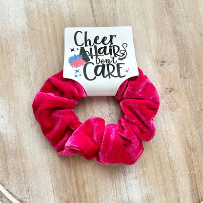 Pink scrunchie on a wooden surface with a card that says 'Cheerleaders don't care'.