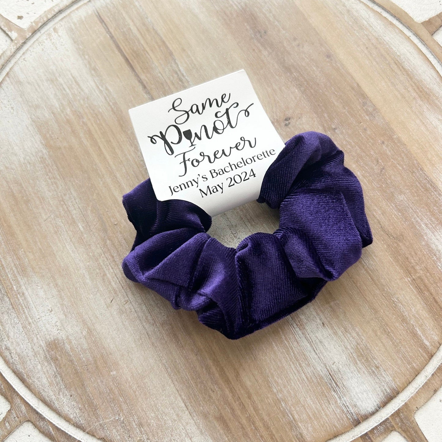 Purple scrunchie on a wooden surface with a card reading 'Same Planet Forever' in the background.