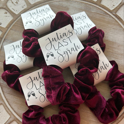 Burgundy scrunchies with personalized labels on a decorative surface