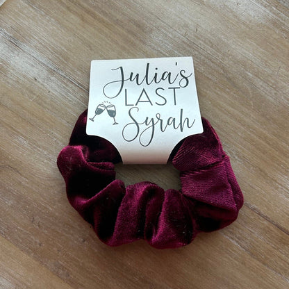 Maroon scrunchie on a wooden surface with a card labeled 'Julia's Last Syrah'.